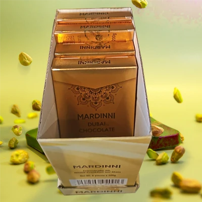 Box of Mardinni Dubai chocolate bars with golden packaging, featuring rich Antep pistachio flavors and surrounded by scattered pistachios.